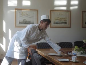 Ein Koch stellt eine Schale mit Kaffeesahne auf einen Tisch mit Kaffeegedeck