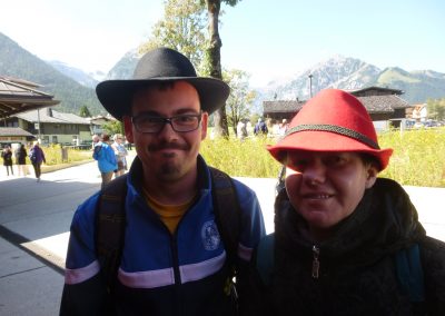 Zwei Personen mit Hut stehen vor Bergen.